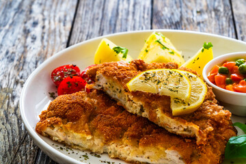Crispy breaded seared chicken cutlet with boiled potatoes and vegetables on wooden table
