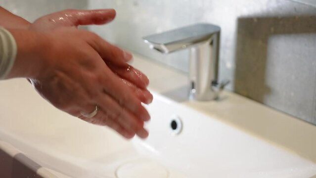Slow Motion. Closeup of Human Hand Under Stream of Pure Water From Tap. Modern faucet in the bathroom. A man washes his hands under running water. Close-up