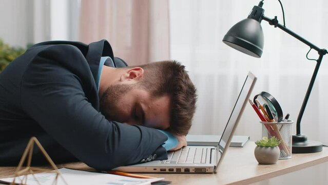 Bored sleepy Caucasian businessman worker working on laptop computer, leaning on hand falling asleep at home office. Exhausted tired freelancer workaholic young man. Employment, occupation, workless