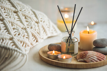 Fototapeta na wymiar Burning candles on bamboo tray, cozy home atmosphere. Relaxation, detention zone in the living or bedroom. Stones, sea shells as decor. Apartment natural aroma diffusor with ocean breeze fragrance.