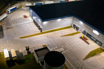 Aerial view of a warehouse of goods at night. Many warehouses and trucks with trailers are in the...