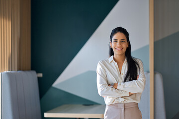 Confident professional young latin business woman company employee, lady executive manager, female worker or entrepreneur looking at camera standing arms crossed in modern office, portrait. - obrazy, fototapety, plakaty