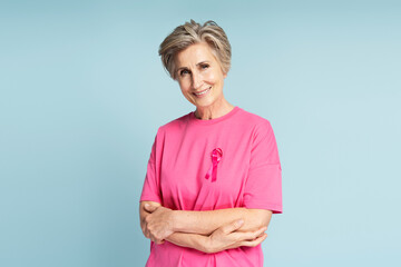 Confident smiling senior woman wearing t shirt with pink ribbon isolated on blue background. Health...