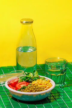Salad bowl on green background with plastic cover near bottle and glass of water