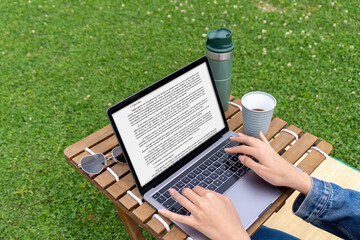 Close-up of the desktop of a woman working remotely with her laptop on a camping chair on the grass. The woman typing on her computer. Remote working and home office