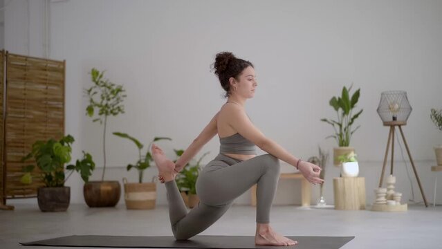 Side view of Latina woman in gray sports wear exercising in class. Yoga One Legged King Pigeon pose or Eka Pada Rajakapotasana. Calm young female heals breathing and meditation with yoga at home. 