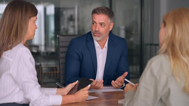 Group of diverse partners mature Latin business man and European business women discussing project with documents at table in office. Team of colleagues professionals business people working together.