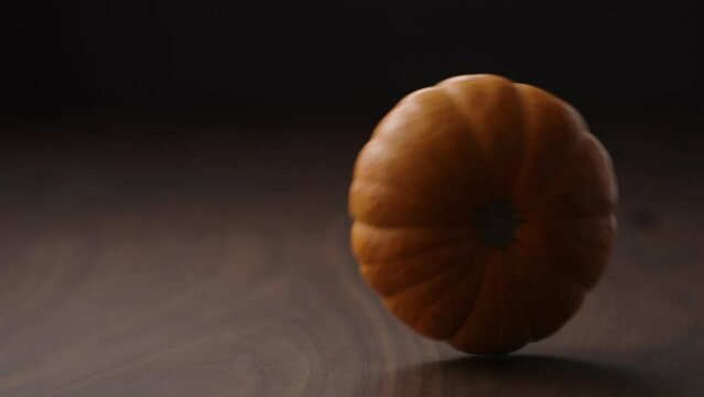 Slow motion small orange pumpkin rolling through frame on walnut table
