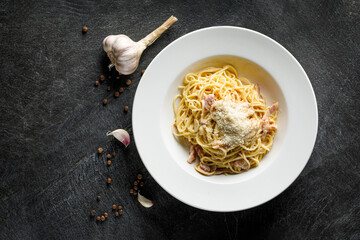 Traditional Italian pasta linguine with bacon and parmisan cheese on a black background in a white plate with garlic and pepper on the background