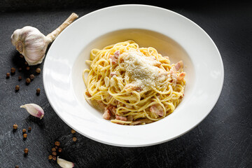 Traditional Italian pasta linguine with bacon and parmisan cheese on a black background in a white plate with garlic and pepper on the background