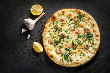Pizza with shrimp and parsley on a black background with lemon, garlic and peppers, top view