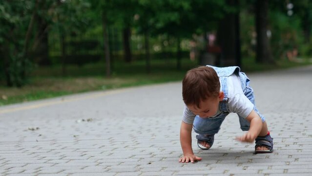 Lovely Caucasian boy sit squatted on the paved road. Adorable kid touches the tiles and crawls on his hands and feet.