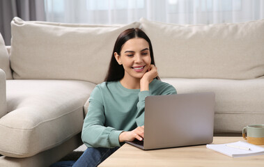 Happy woman working with laptop at coffee table in living room