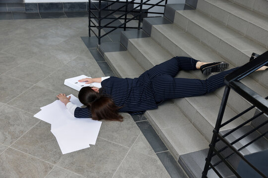 Unconscious woman with scattered folder and papers lying on floor after falling down stairs indoors