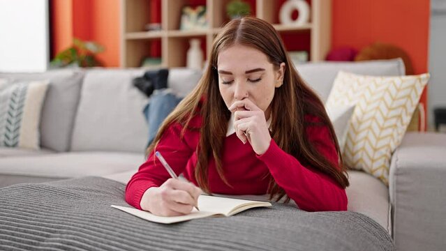 Young hispanic woman writing on notebook lying on sofa at home