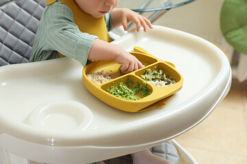 Little baby eating healthy food in high chair indoors, closeup
