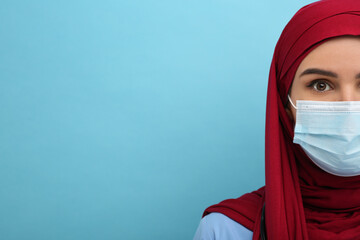 Muslim woman wearing hijab, medical uniform and protective mask on light blue background, closeup. Space for text