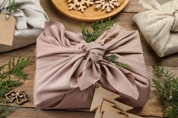 Furoshiki technique. Gift packed in fabric, thuja branches and festive decor on wooden table, closeup