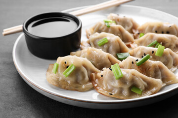 Delicious gyoza (asian dumplings) with green onions, soy sauce and chopsticks on gray table, closeup