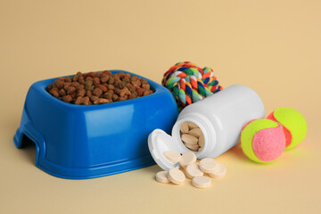 Bottle with vitamins, toys and dry pet food in bowl on beige background