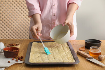 Making delicious baklava. Woman buttering dough at wooden table, closeup - Powered by Adobe