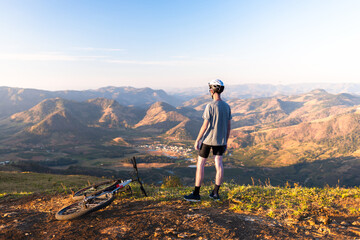 Cyclist resting with his mountain bike while admiring the mountainous landscape in the background.