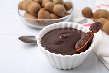 Bowl of tamarind sauce and fresh pods on light table, closeup