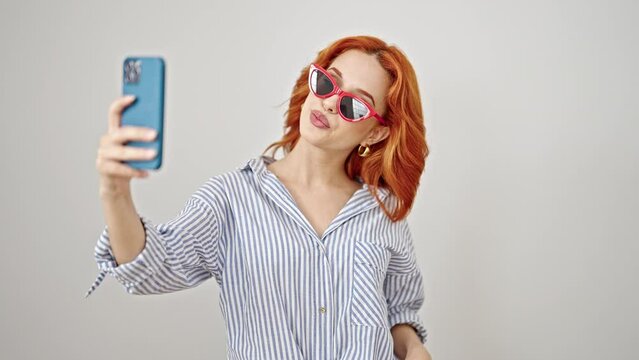Young redhead woman wearing sunglasses make selfie by smartphone over isolated white background