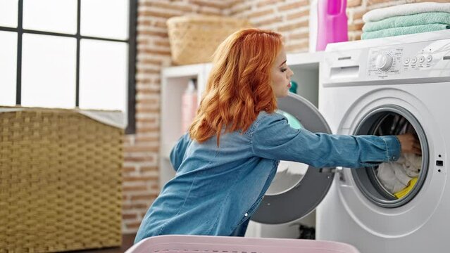 Young redhead woman washing clothes holding dirty clothes at laundry room