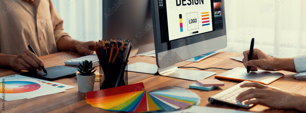 Poster Graphic designer work on computer laptop and with graphic drawing pen while brainstorming unique design with professional graphic team in modern digital studio workplace. Panorama shot. Scrutinize
