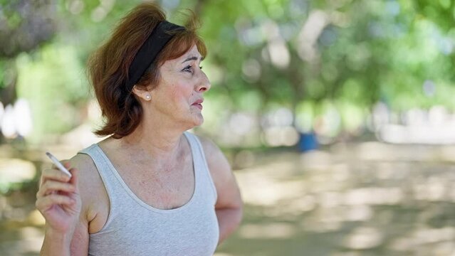 Middle age woman smiling confident smoking at park