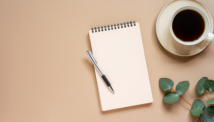 Flat lay, top view office table desk. Feminine workspace with paper notebook, pen, cup of coffee and eucalyptus leaf on beige background with copy space. Business concept
