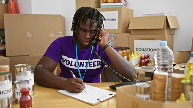 African american man volunteer talking on telephone writing on clipboard at charity center