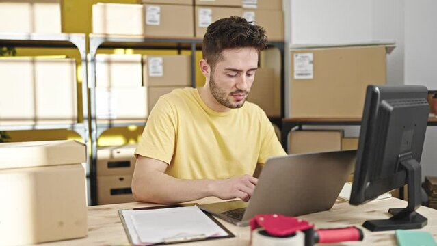 Young hispanic man ecommerce business worker using laptop writing on document at office