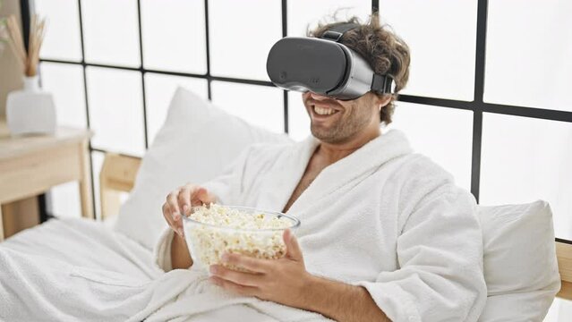 Young hispanic man watching movie using virtual reality glasses at bedroom