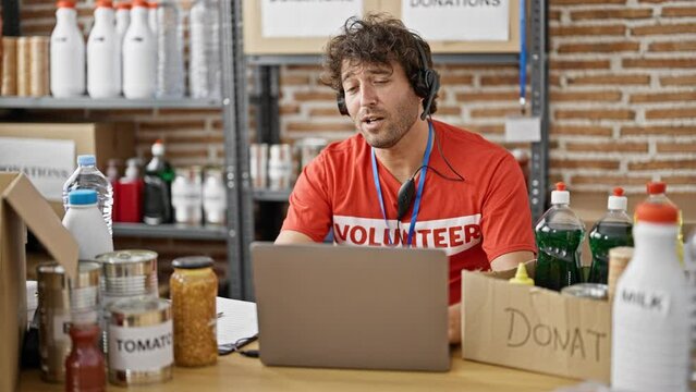 Young hispanic man volunteer writing on clipboard having video call at charity center