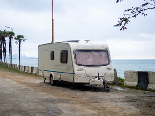 Old trailer in the parking lot. Vacationers savages on the sea.