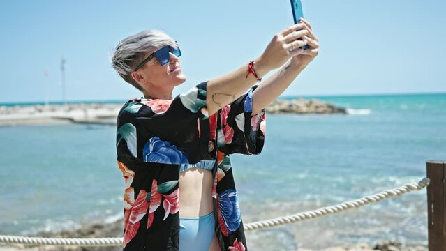 Young woman tourist wearing bikini and sunglasses make selfie by smartphone at beach