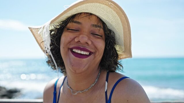 Young beautiful latin woman tourist smiling confident wearing summer hat at seaside