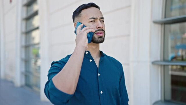 Young hispanic man speaking on the phone at street