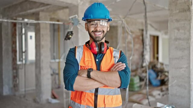Young hispanic man builder smiling confident with crossed wearing hardhat at construction site