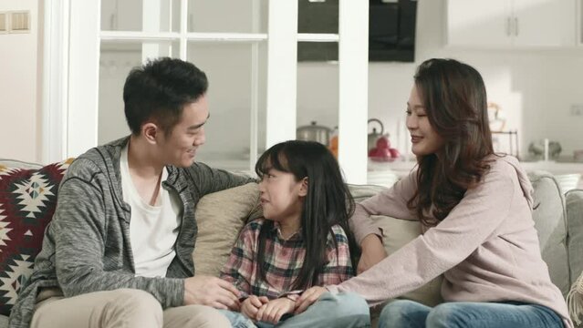 young asian couple sitting on family couch at home chatting with daughter