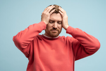 Portrait of sad man having life troubles holding head with suffering face on studio blue background. Frustrated, confused male with headache, life problems, midlife crisis. Stress, panic, desperation. - obrazy, fototapety, plakaty