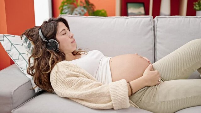 Young pregnant woman listening to music sleeping on sofa at home