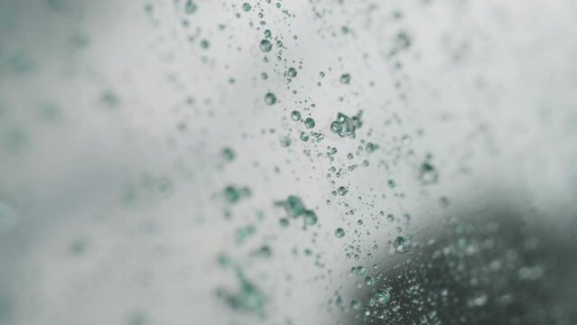 Slow motion handheld shot of rain drops beading on hydrophobic car glass