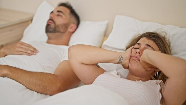 Man and woman couple lying on bed covering ears for snore at bedroom