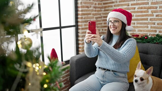Young hispanic woman with chihuahua dog taking photos of christmas tree at home