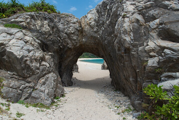岩のトンネルの向こうに広がる白い砂浜とエメラルドグリーンの海