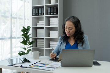 Retired businesswoman or senior executive looking at documents and recordings of online webinars on laptop computer. meeting to plan Analyze economic plans, taxes, office investments.