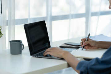 Fototapeta premium Young businessman, asian office worker sitting working on laptop computer in office data research concept note taking online learning